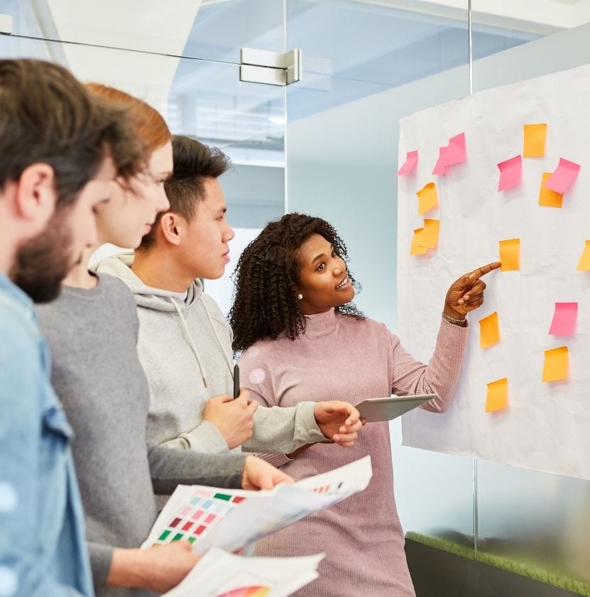 A diverse group of professionals brainstorming with colorful sticky notes on a whiteboard in a modern office setting.