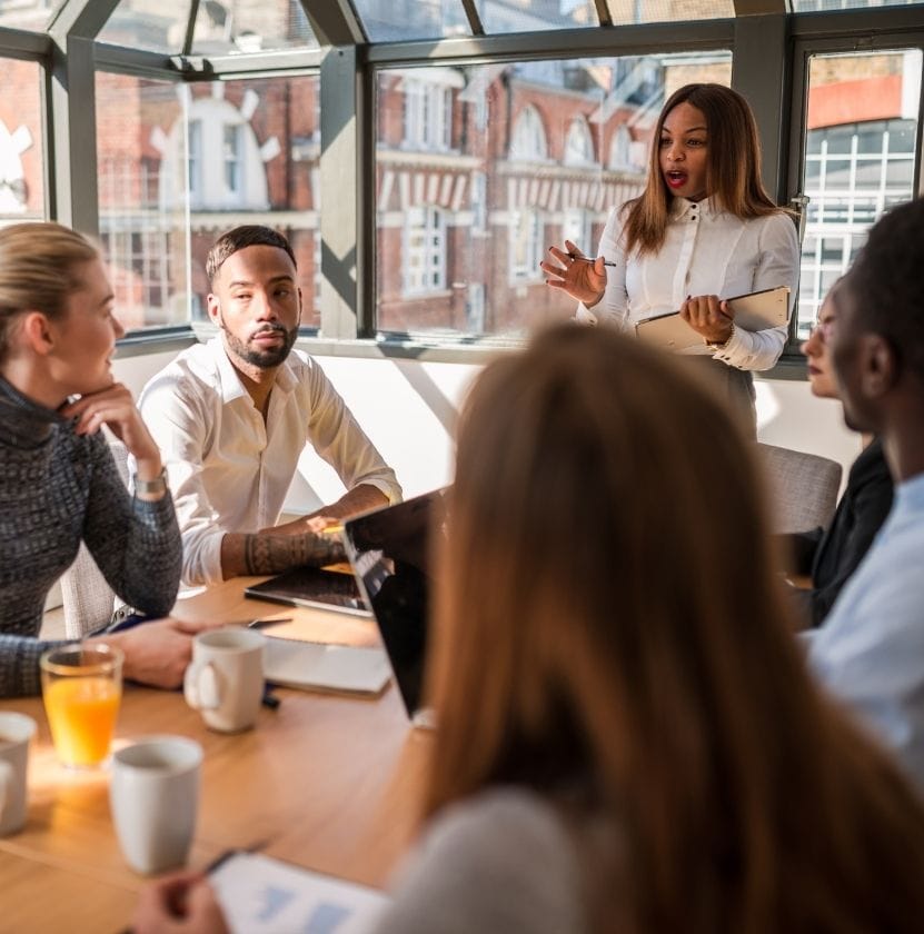 Businesswoman leading a strategic team meeting in a modern glass-walled office with five diverse colleagues.