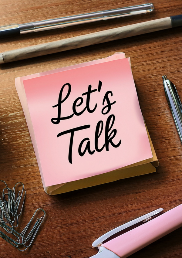 Pink sticky note with “Let’s Talk” message on a wooden desk with office supplies.